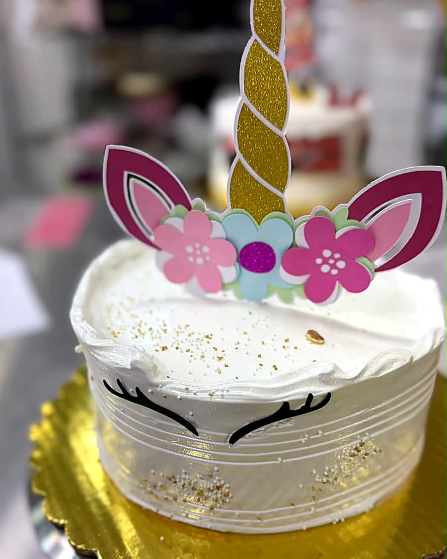 A unicorn cake with a gold horn, closed eyes with lashes, and a crown of pink and blue flowers.
